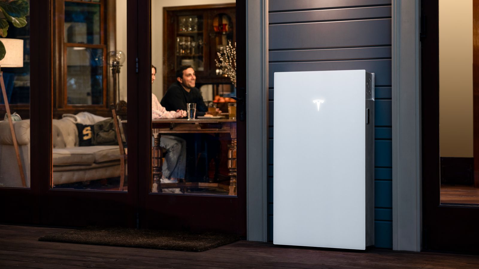 Tesla Powerwall 3 ’s avonds aan de gevel terwijl het huis verlicht is: ontladen in dure uren