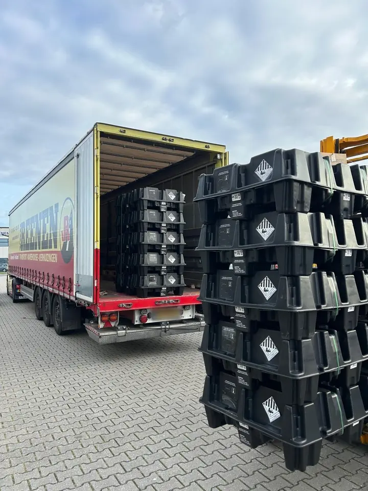 Vrachtwagen met geopende oplegger en een stapel uitgeladen Tesla Powerwalls ervoor bij Thuisbatterijplaza
